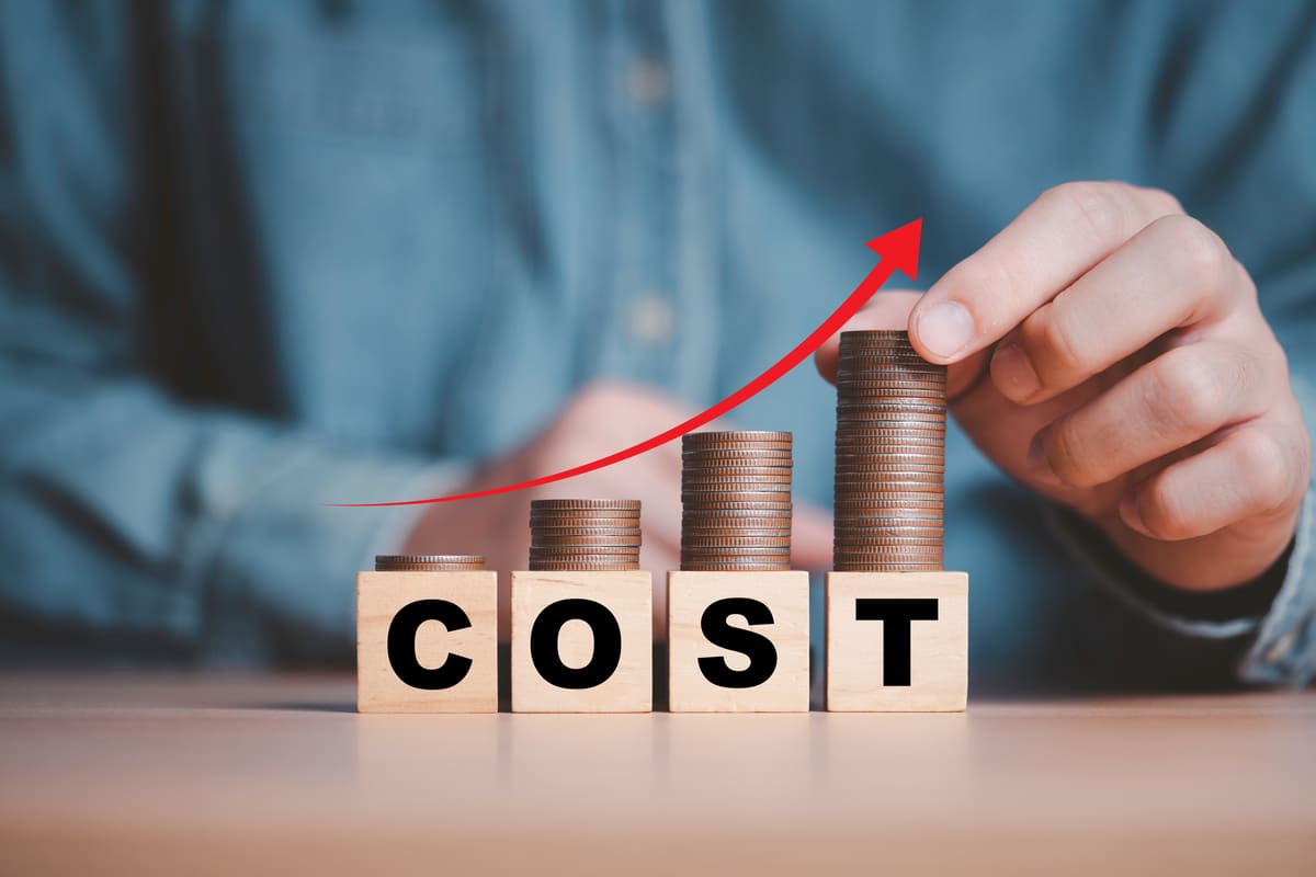 コストと書かれた積み木と硬貨を積んでいる手