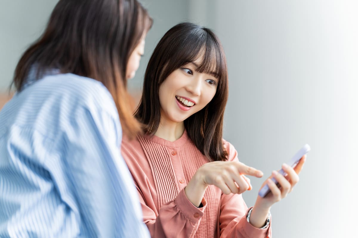 スマホを見て楽しそうに話す2人のビジネスウーマン